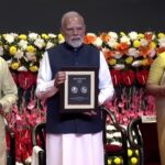 PM Modi holding RSS 100 years commemorative stamp and 100 rupees coin during centenary celebration
