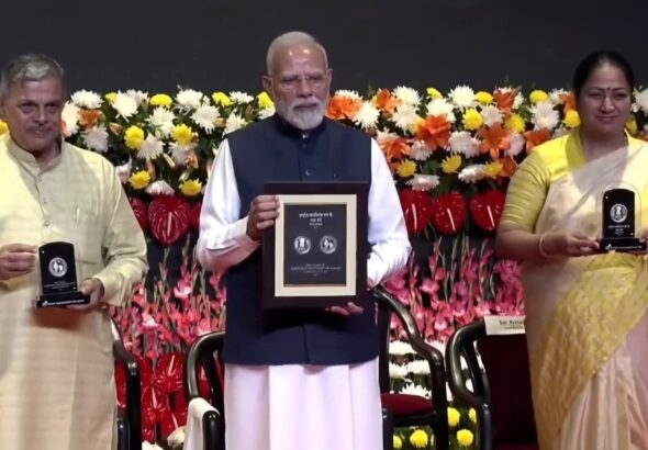 PM Modi holding RSS 100 years commemorative stamp and 100 rupees coin during centenary celebration