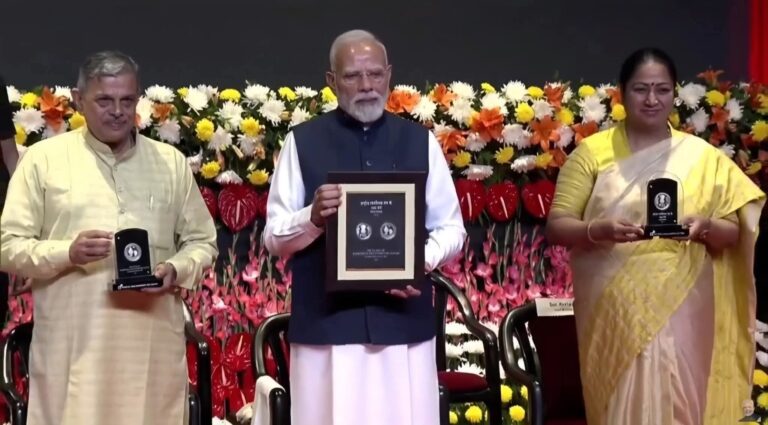 PM Modi holding RSS 100 years commemorative stamp and 100 rupees coin during centenary celebration